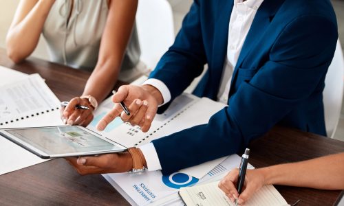 Finance, tablet and hands writing in a notebook during a meeting with team working in collaboration.